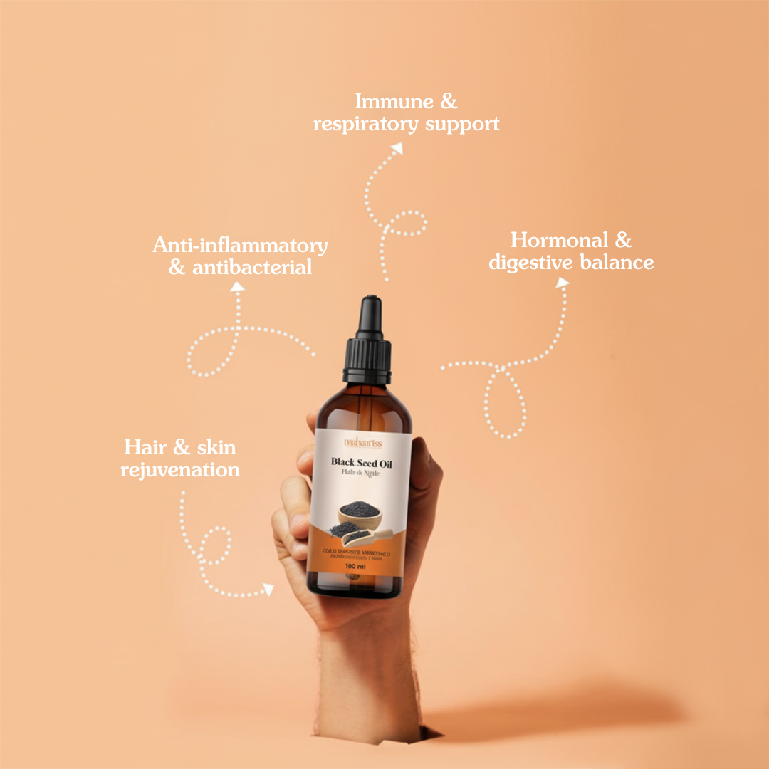 Hand holding a bottle of black seed oil with health benefits text on a peach background