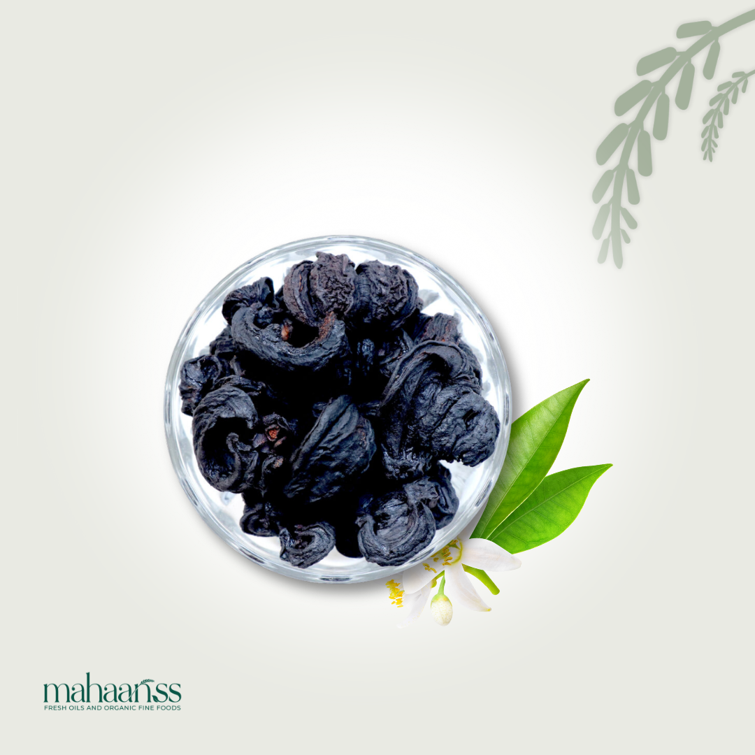 Bowl of dried black karaka fruit with green leaves and white flower on a light background