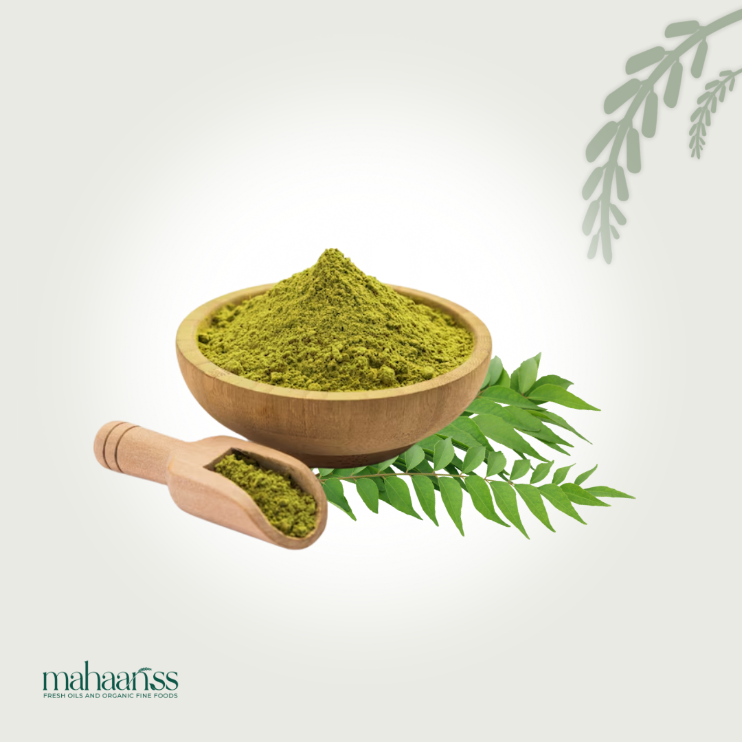 Natural curry powder in a wooden bowl and scoop on curry leaves, isolated background